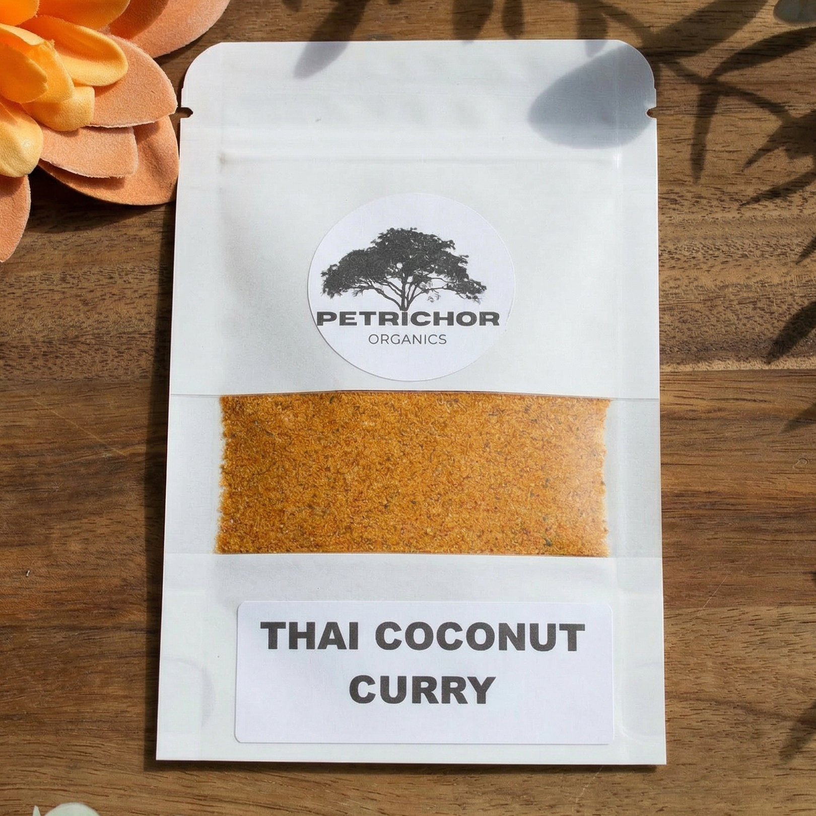 Petrichor Organics Thai Coconut Curry Organic Seasoning Packet on a wooden surface with flowers and leaves.
