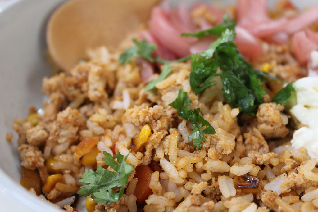Close-up of a bowl of fried rice with ground meat, vegetables, and herbs.